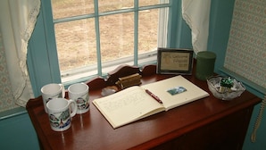 A wooden desk with a notebook, two mugs, a framed sign, a telephone, and a decorative bowl.