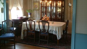 A dining room with a table set for four, surrounded by wooden chairs. A chandelier hangs above the table, and a vase with flowers is on the table.