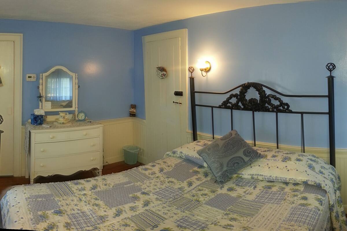 Een slaapkamer met een bed, een kaptafel, een spiegel en een wandlamp.