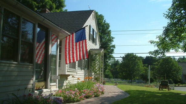 A house with a porch, American flags, and a pathway leading to a bench.