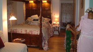 A four-poster bed with floral bedding, two bedside lamps, and a wooden floor.