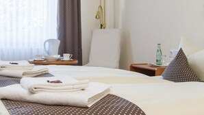 A hotel room with two beds, each with a neatly folded white towel, a pillow, and a bedside table with a cup and a bottle. - Landhotel Elkemann (Ahaus)