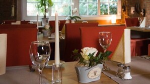 A restaurant setting with tables set for dining, featuring candles, wine glasses, and a vase with flowers. - Landhotel Elkemann (Ahaus)