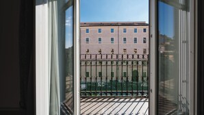 A view through a window with a metal balcony railing, a building with multiple windows, and a clear sky. - Affittacamere Centro Cavour (Rome)