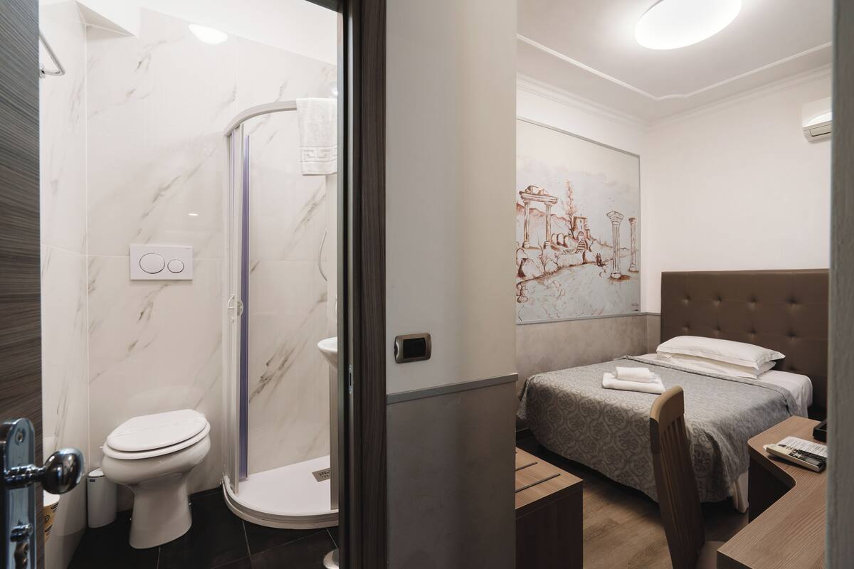 A modern bathroom with a shower, toilet, and a bed with a headboard and a bedside table.