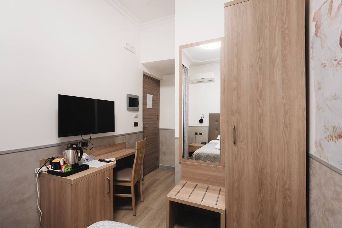 A hotel room with a wooden desk, a flat-screen TV, a bed with a wooden headboard, and a large mirror.
