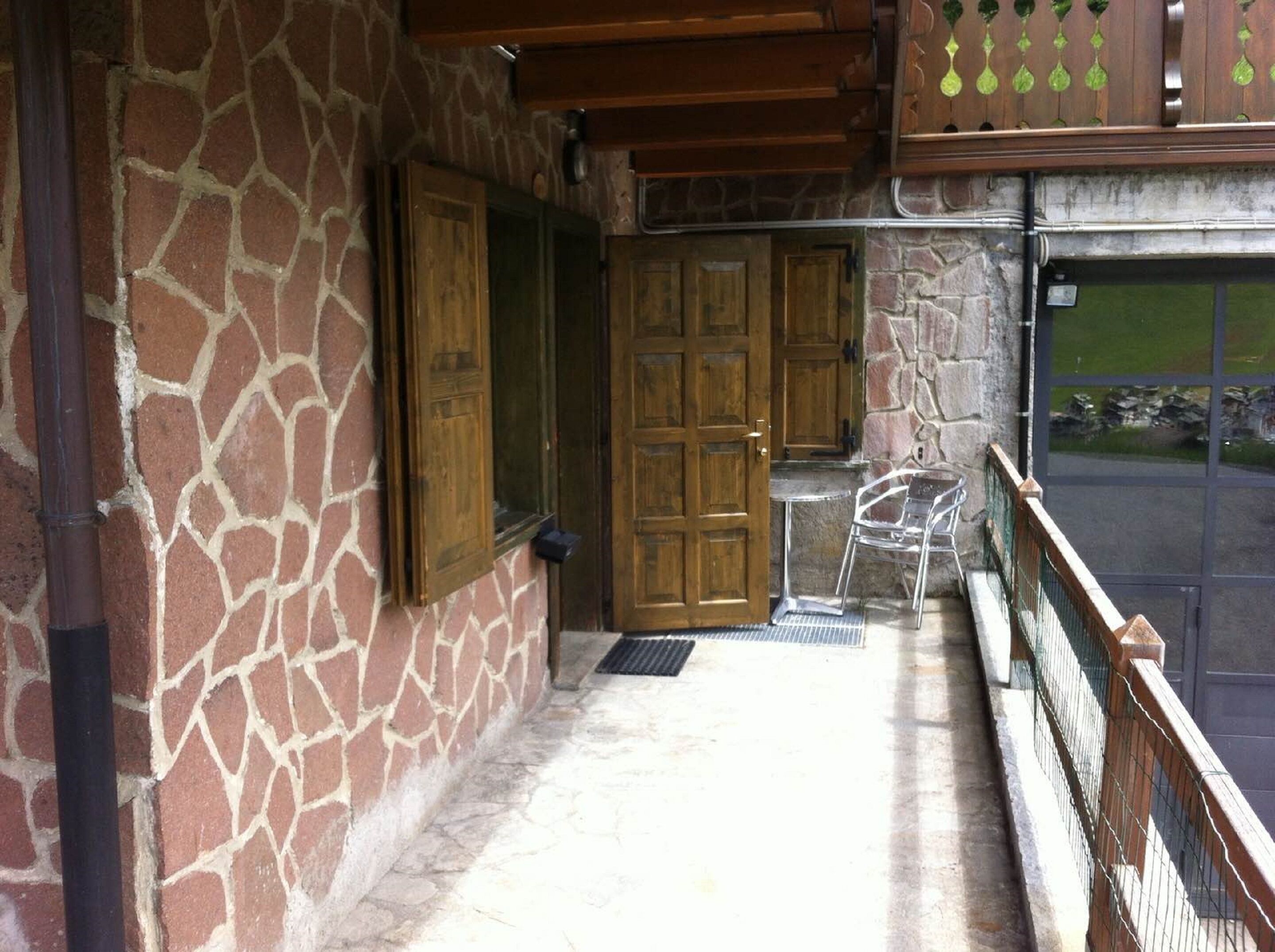 A stone wall with a wooden door, a metal chair, and a glass door leading to a view.