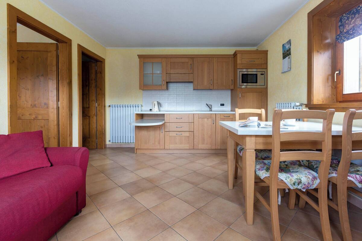 A compact kitchen with wooden cabinets, a microwave, and a dining area with a table and chairs.