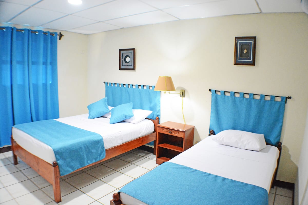 Une chambre d’hôtel avec deux lits, chacun doté de draps bleus et d’oreillers blancs, une table de chevet avec une lampe et une petite étagère.
