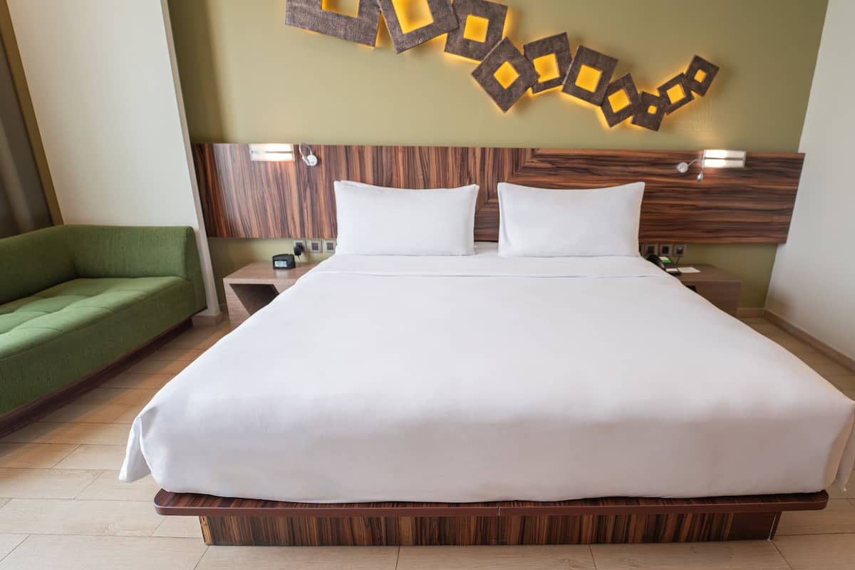 A large bed with white linens, a wooden headboard, and a green sofa.