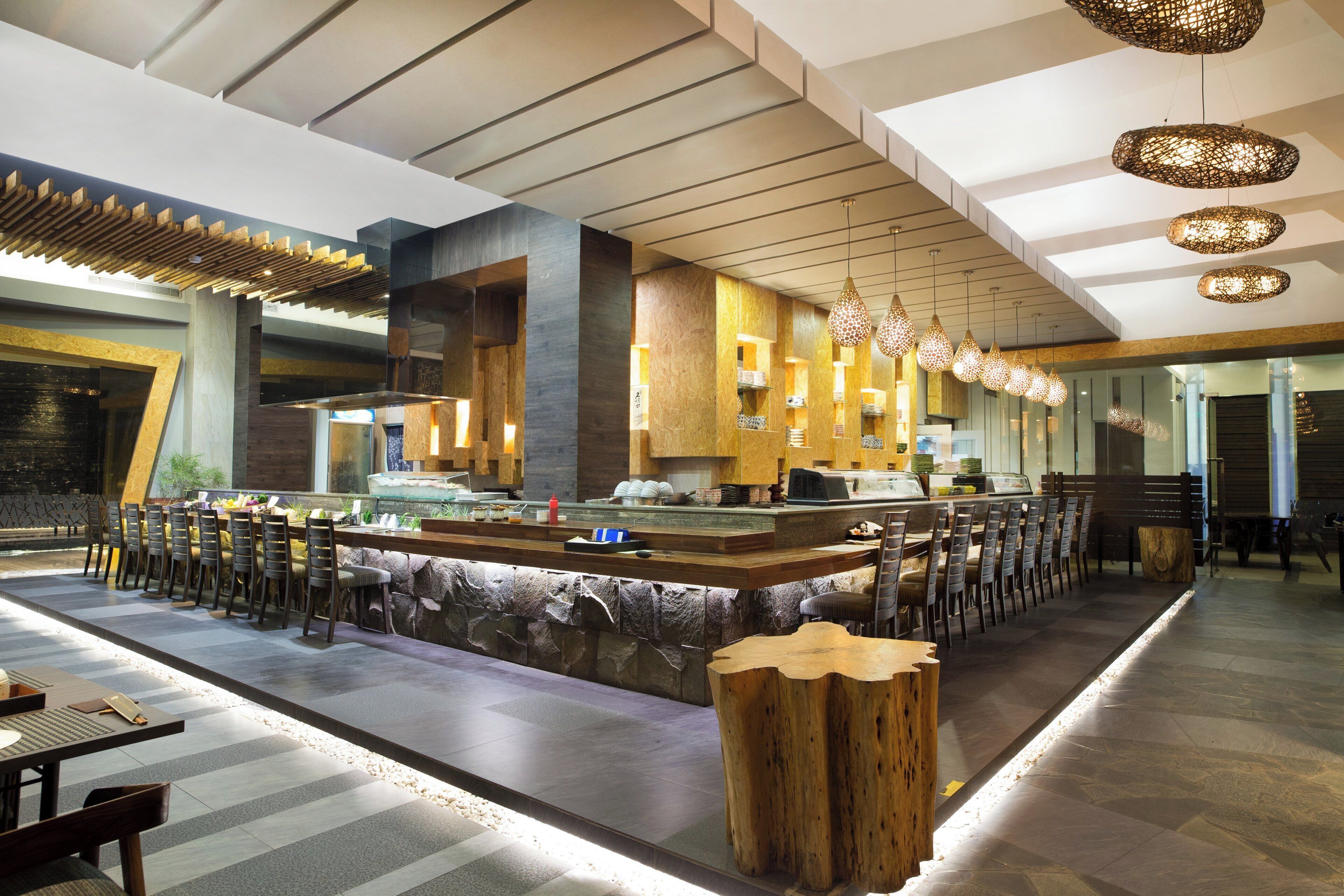 A modern restaurant interior with a central bar, seating area, and decorative lighting.