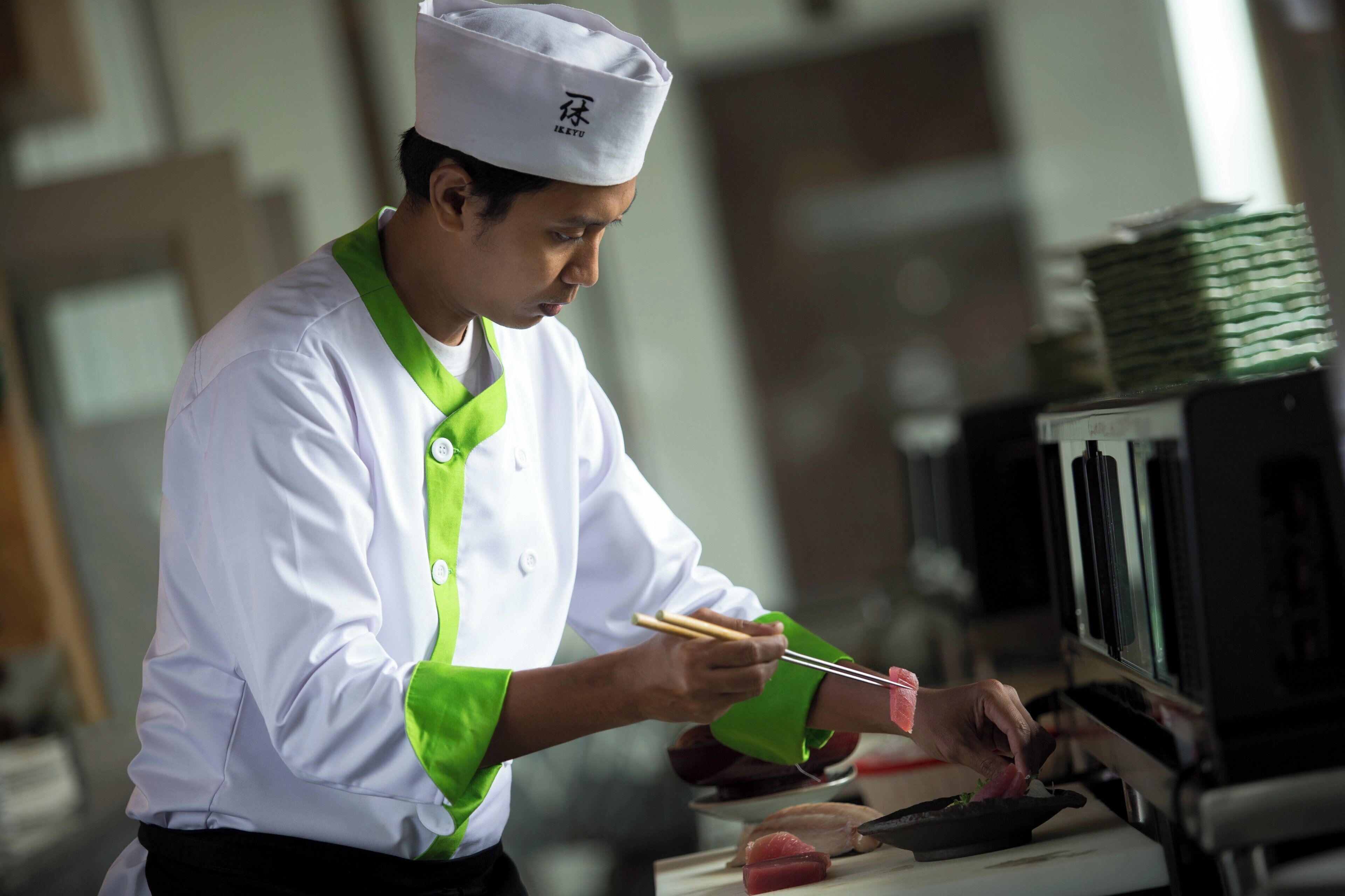 A chef in a white uniform with green accents preparing food.