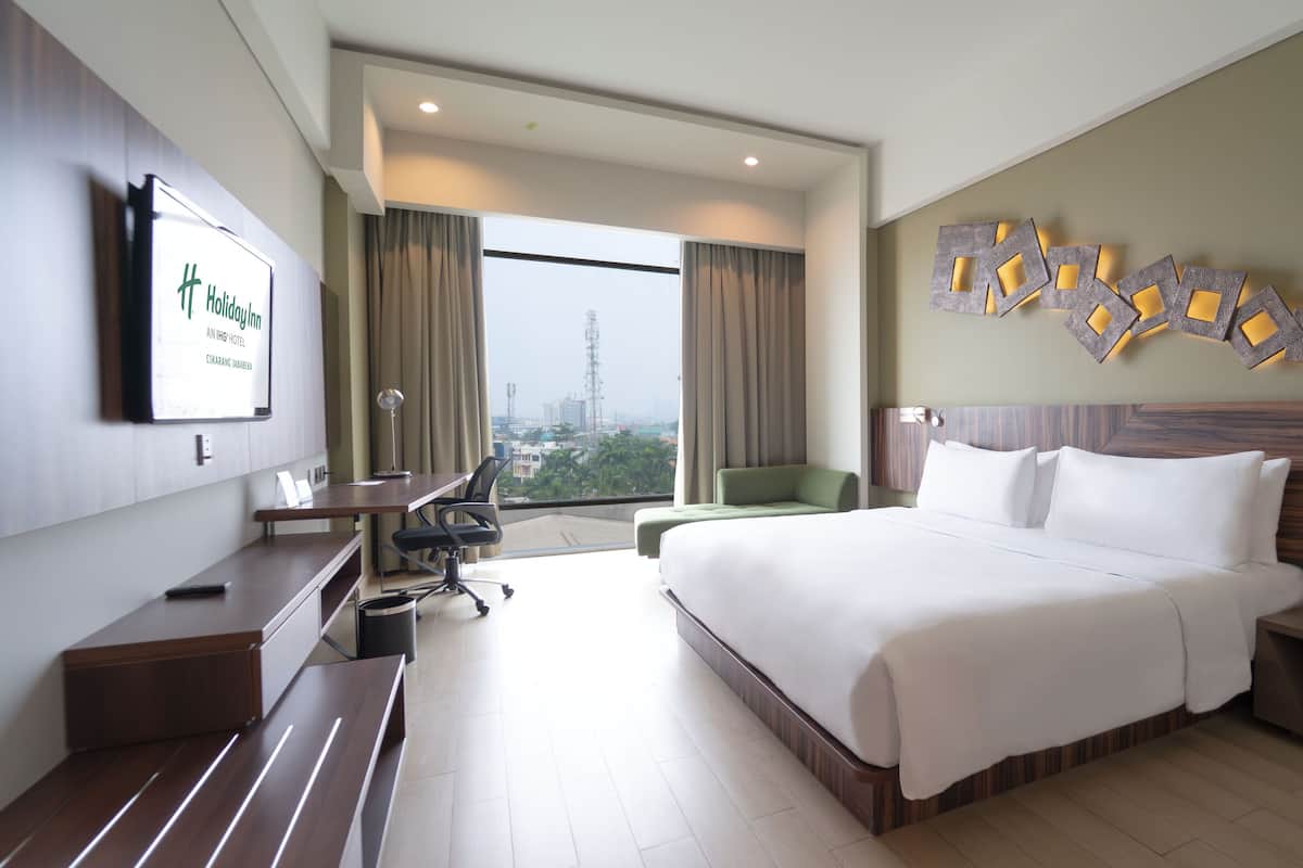 A hotel room with a large bed, a desk, a chair, a small table, and a TV on the wall.