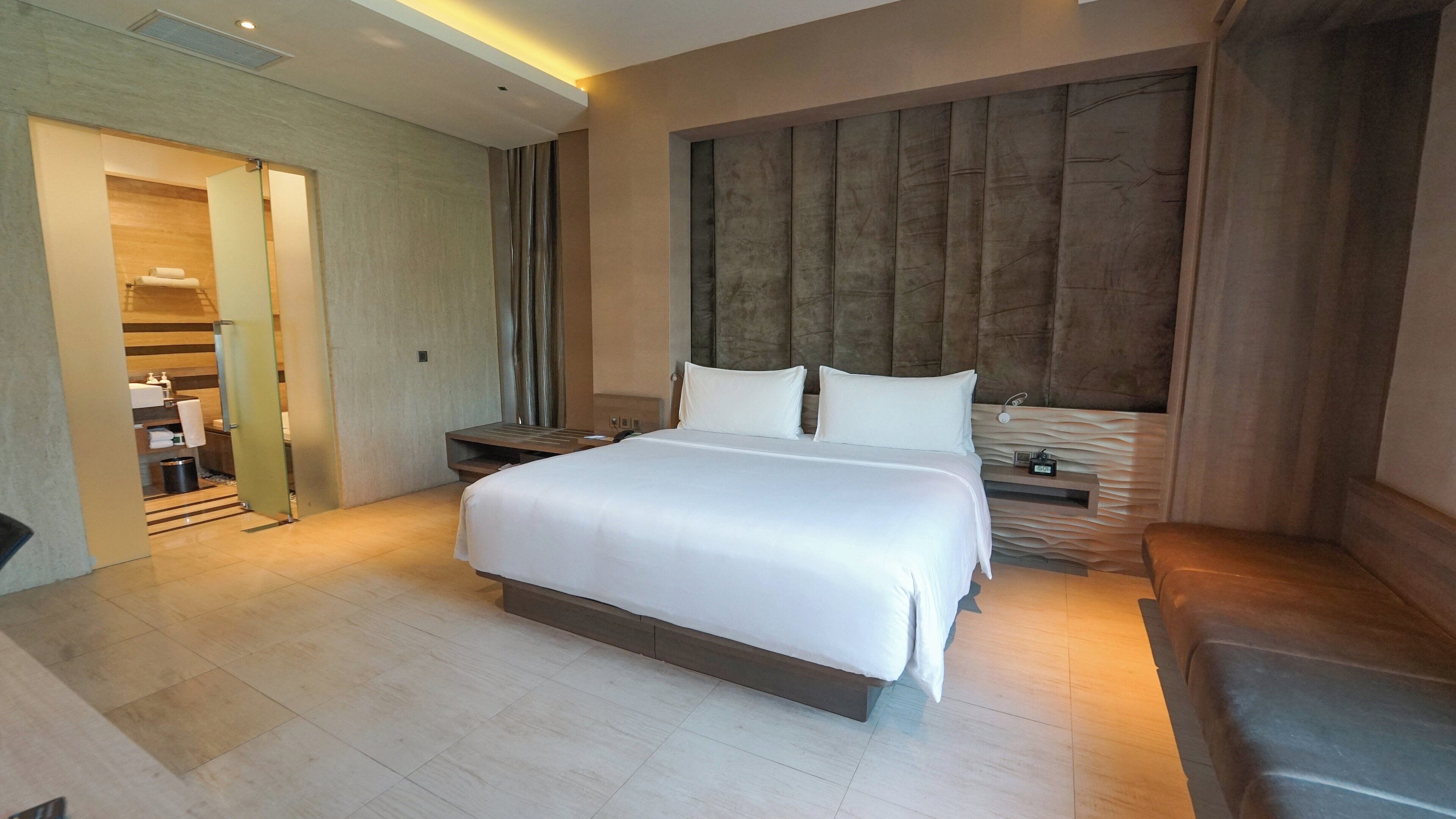 Ein modernes Hotelzimmer mit einem großen Bett, einem Holzkopfteil, einem Nachttisch und einer eingebauten Bank.