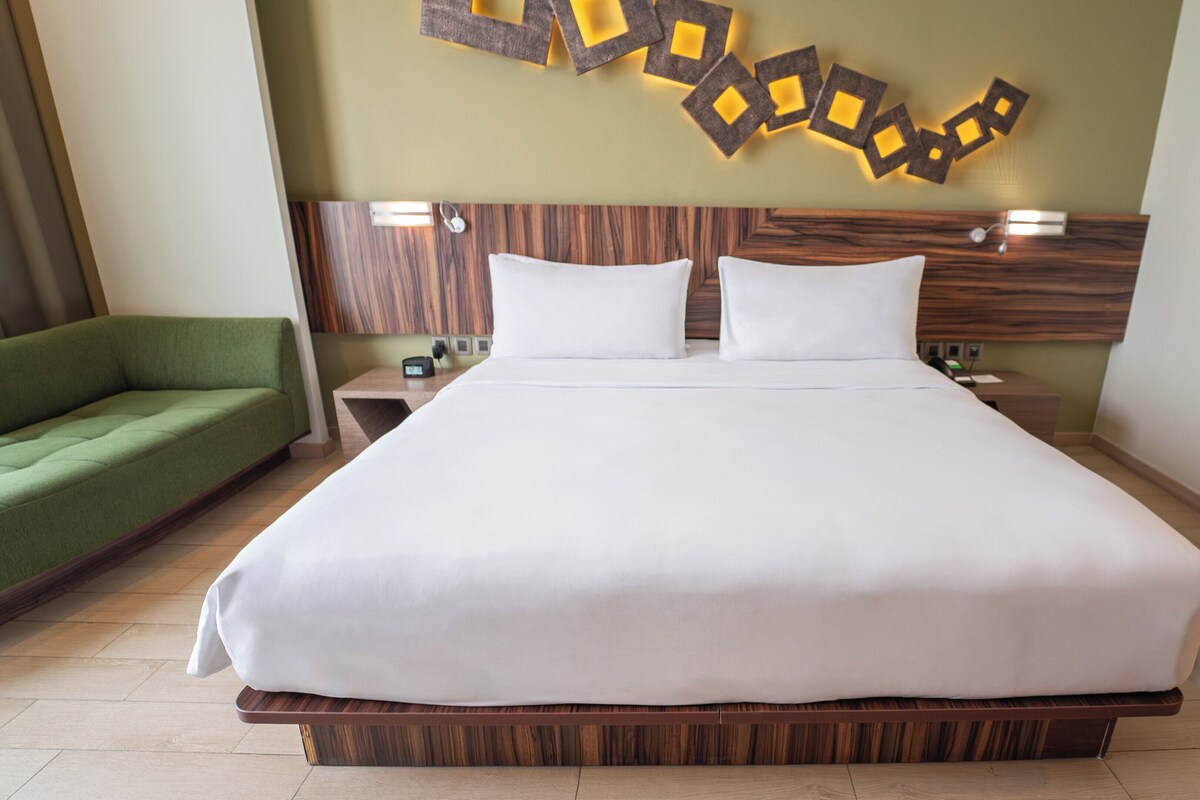 A large bed with white linens, a wooden headboard, and a green sofa.