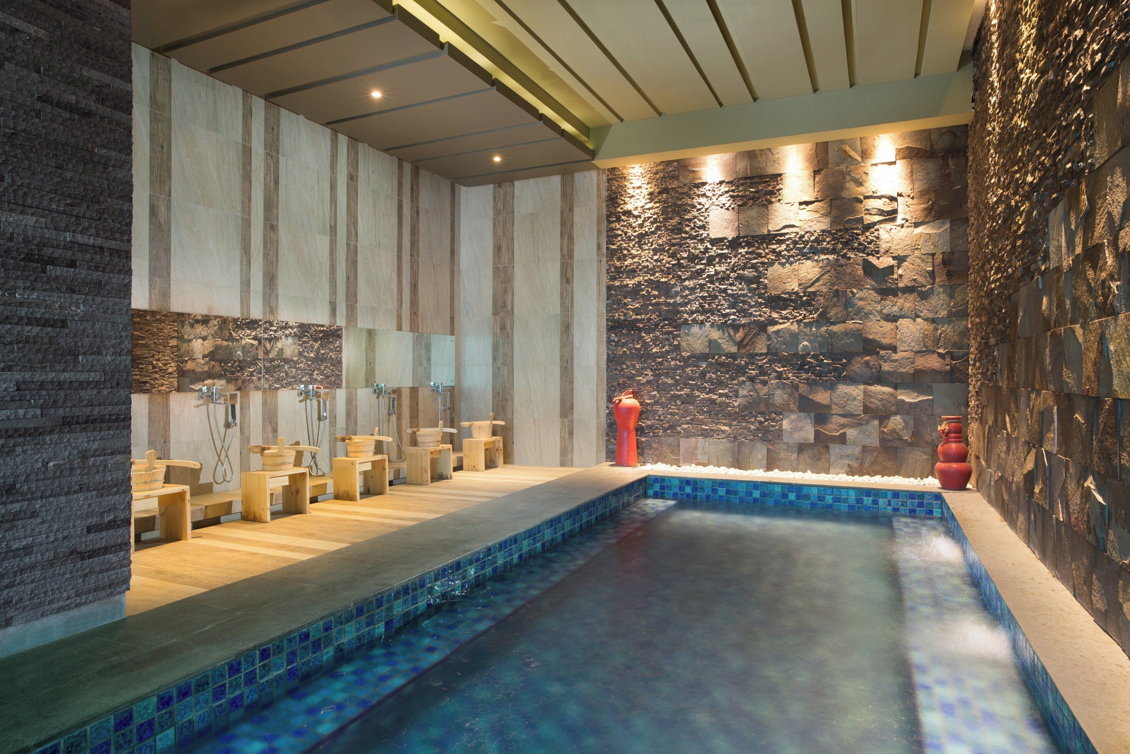 A spa area with a stone wall, a pool, wooden benches, and a stone fire feature.