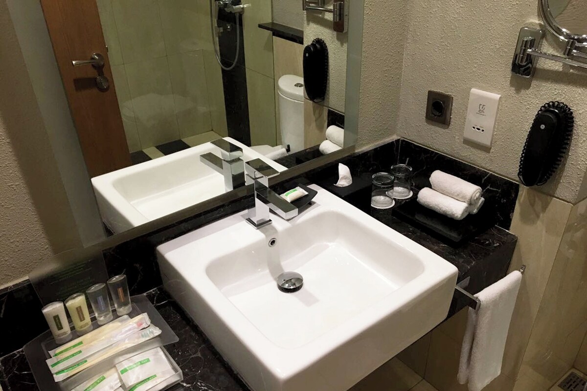 A bathroom with a white sink, a mirror, a towel rack, and toiletries on the counter.