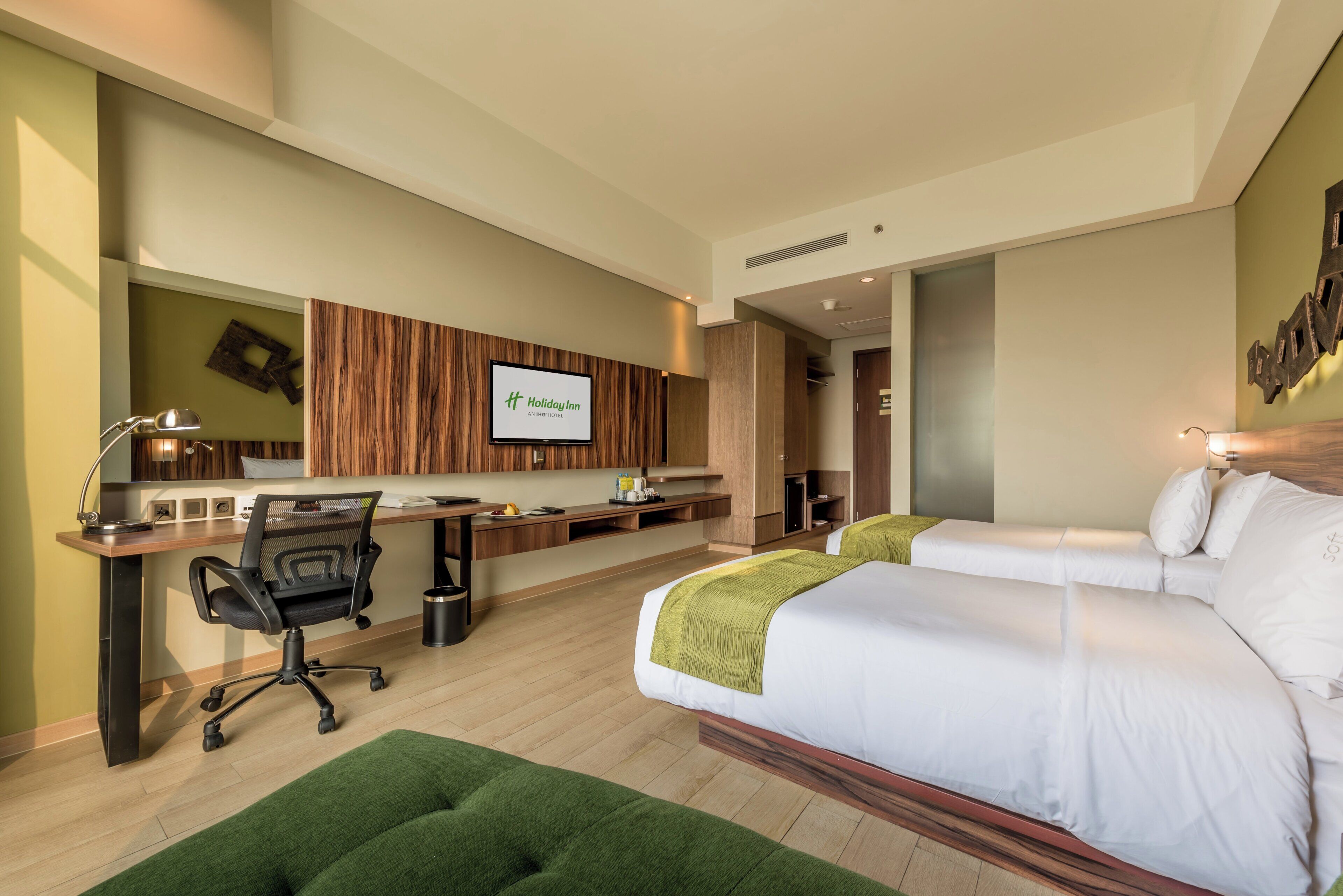 A hotel room with a bed, desk, chair, and a TV displaying the Holiday Inn logo.