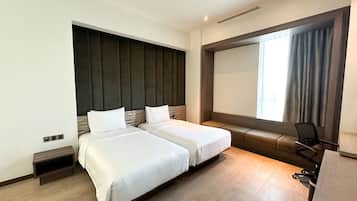 Habitación de hotel con dos camas, un escritorio, una silla, un ventanal grande con cortinas y televisión incorporada.
