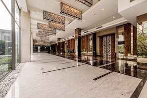 A spacious lobby with a polished marble floor, modern hanging light fixtures, and large windows offering a view of the outdoors. - Holiday Inn Cikarang Jababeka by IHG (Cikarang)