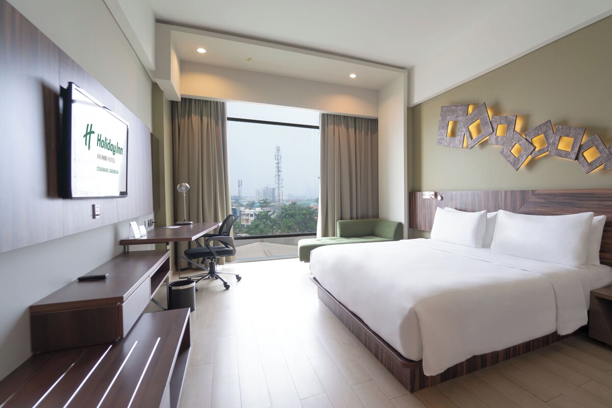 A hotel room with a large bed, a desk, a chair, a small table, and a TV on the wall.