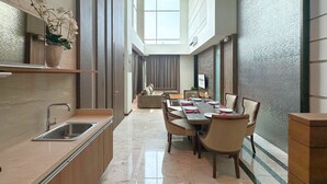 A modern hotel dining area with a long table set for a meal, a kitchen area with a sink, and a decorative plant. - Holiday Inn Cikarang Jababeka by IHG (Cikarang)