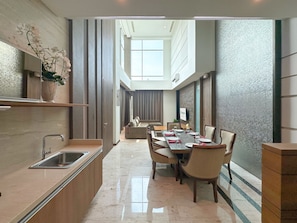 A modern hotel dining area with a long table set for a meal, a kitchen area with a sink, and a decorative plant.