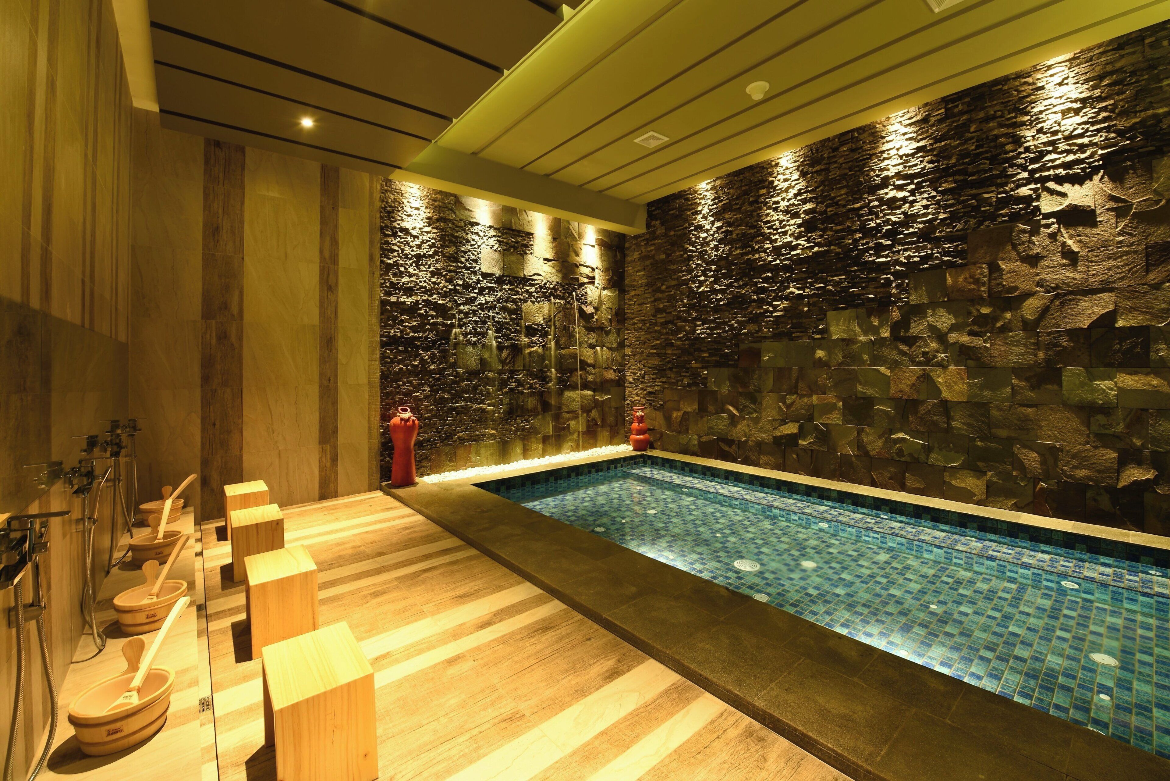 Un área de spa con piscina, escalones de madera y una pared de piedra.
