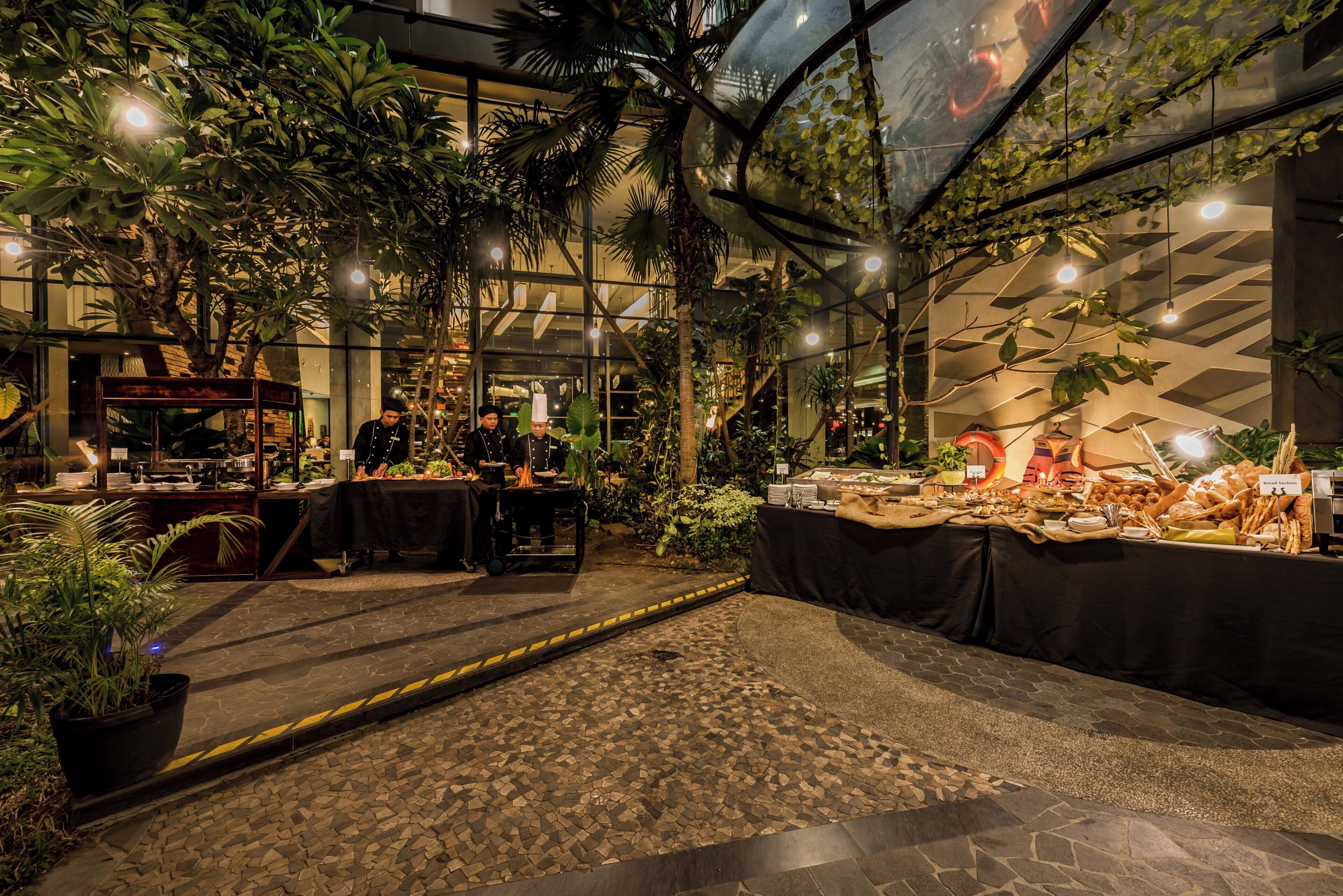 Un espacio interior con temática tropical, que incluye un bufé con diversas opciones de comida y un chef trabajando.