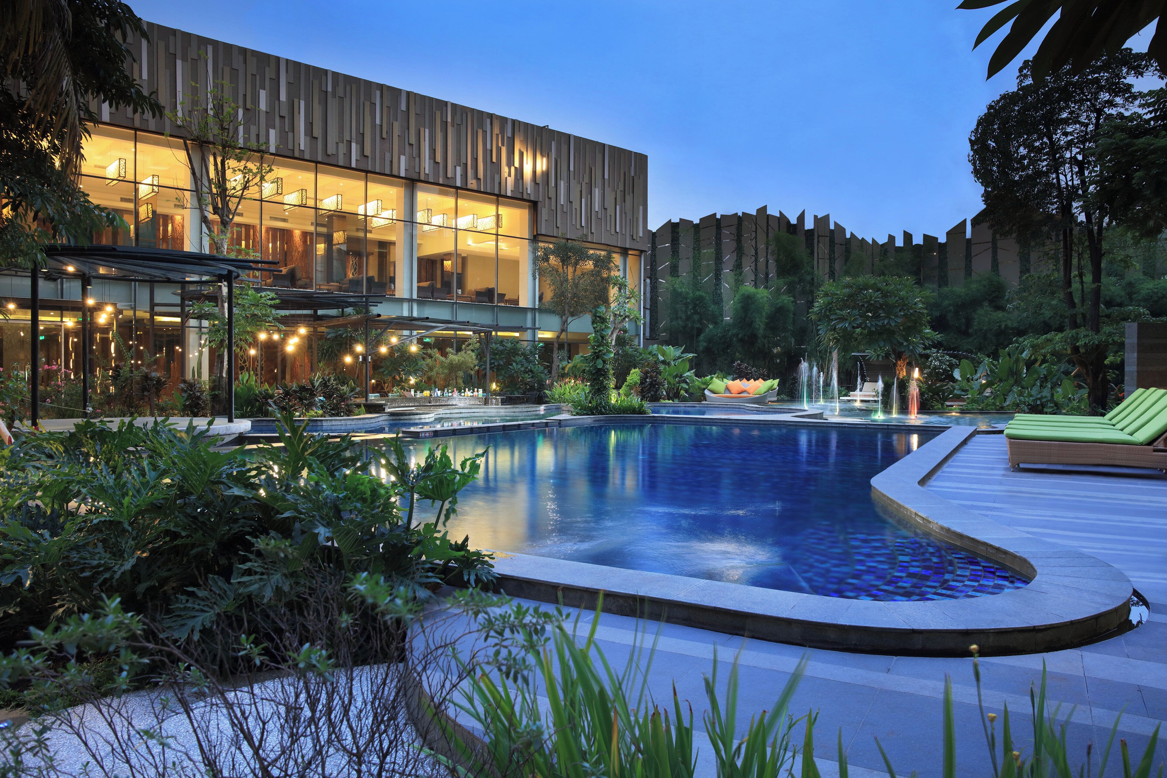 A modern building with a pool, surrounded by lush greenery and a well-maintained garden.