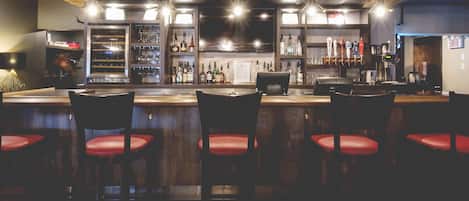 Una zona de bar con mostrador, taburetes y estantes llenos de botellas.