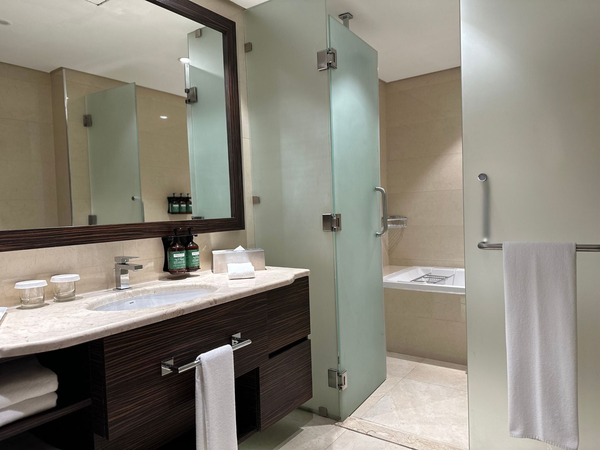 A modern bathroom with a marble sink, a large mirror, a glass shower enclosure, and a towel rack.