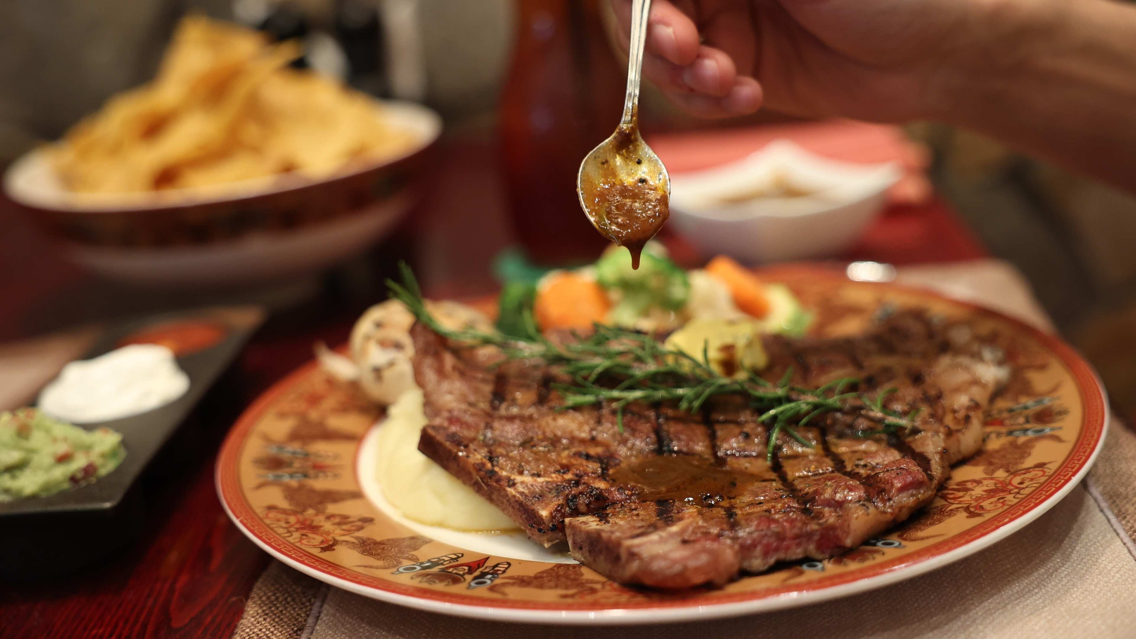 Bife com guarnição de ervas em um prato, acompanhado de batatas fritas e uma tigela de molho.