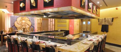 A restaurant with a central island, multiple dining tables, and chairs.