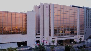 Un hotel moderno con fachada de vidrio, varias banderas y un cartel destacado que dice "CROWNE PLAZA".