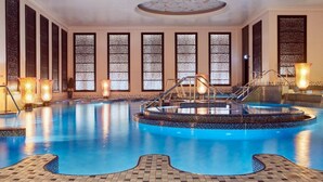 An indoor swimming pool with a central hot tub, surrounded by tiled flooring and decorative lighting. - Crowne Plaza Kuwait Al Thuraya City by IHG (Farwaniya)