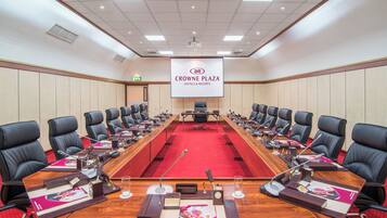 A conference room with a long table, multiple chairs, microphones, and a screen displaying the Crowne Plaza Hotels & Resorts logo.