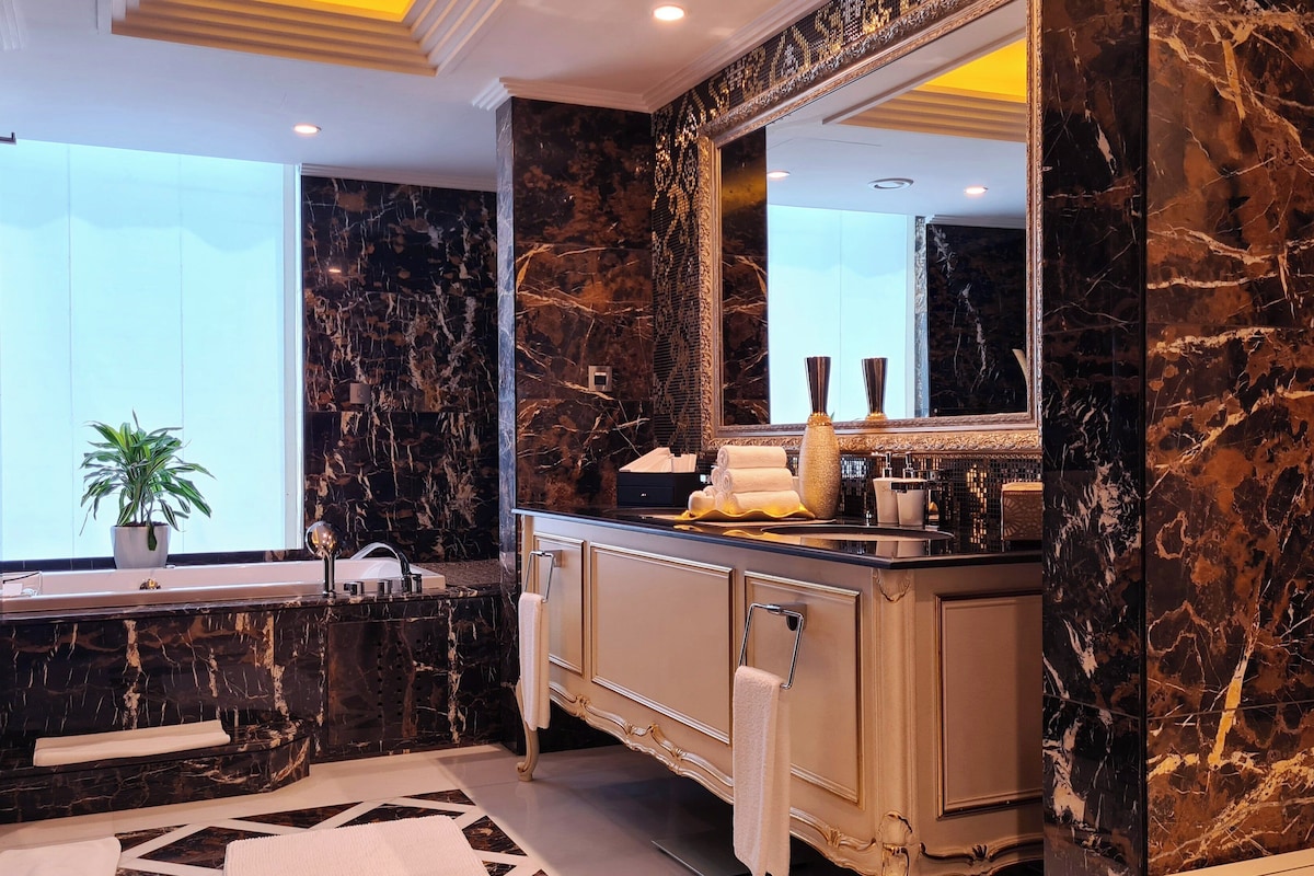 A luxurious bathroom with marble walls, a large mirror, a sink, and a potted plant.