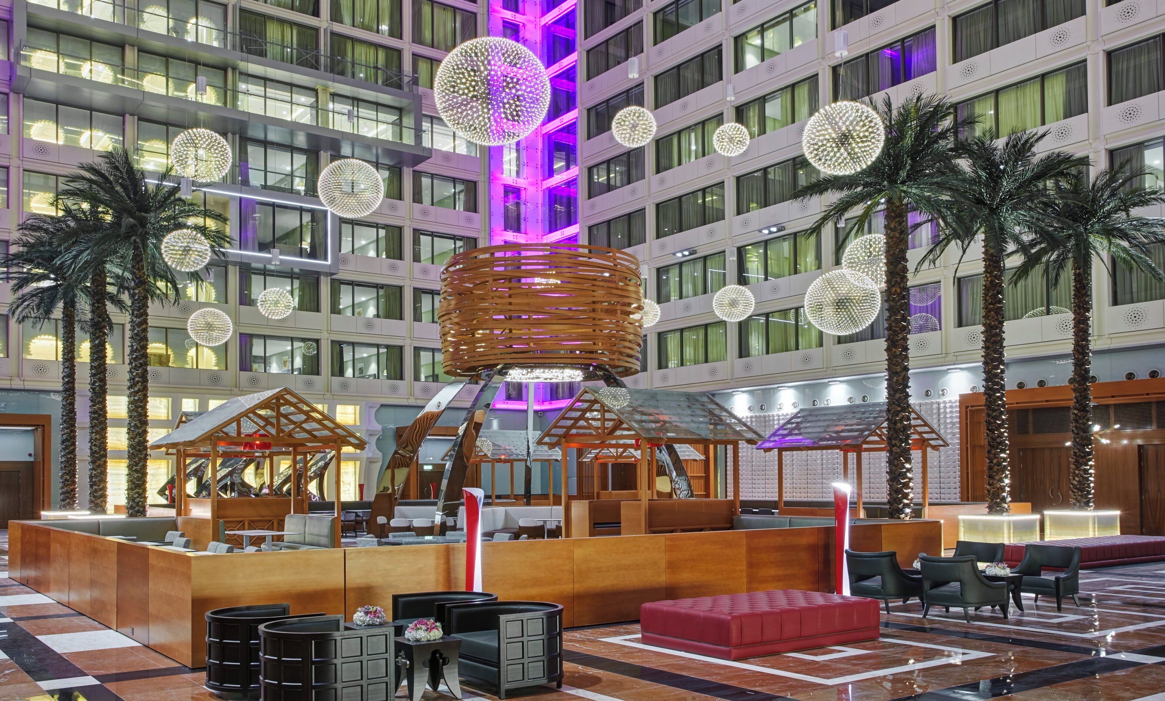 Un hall d’hôtel moderne avec un comptoir d’accueil, des espaces de détente et un éclairage décoratif.