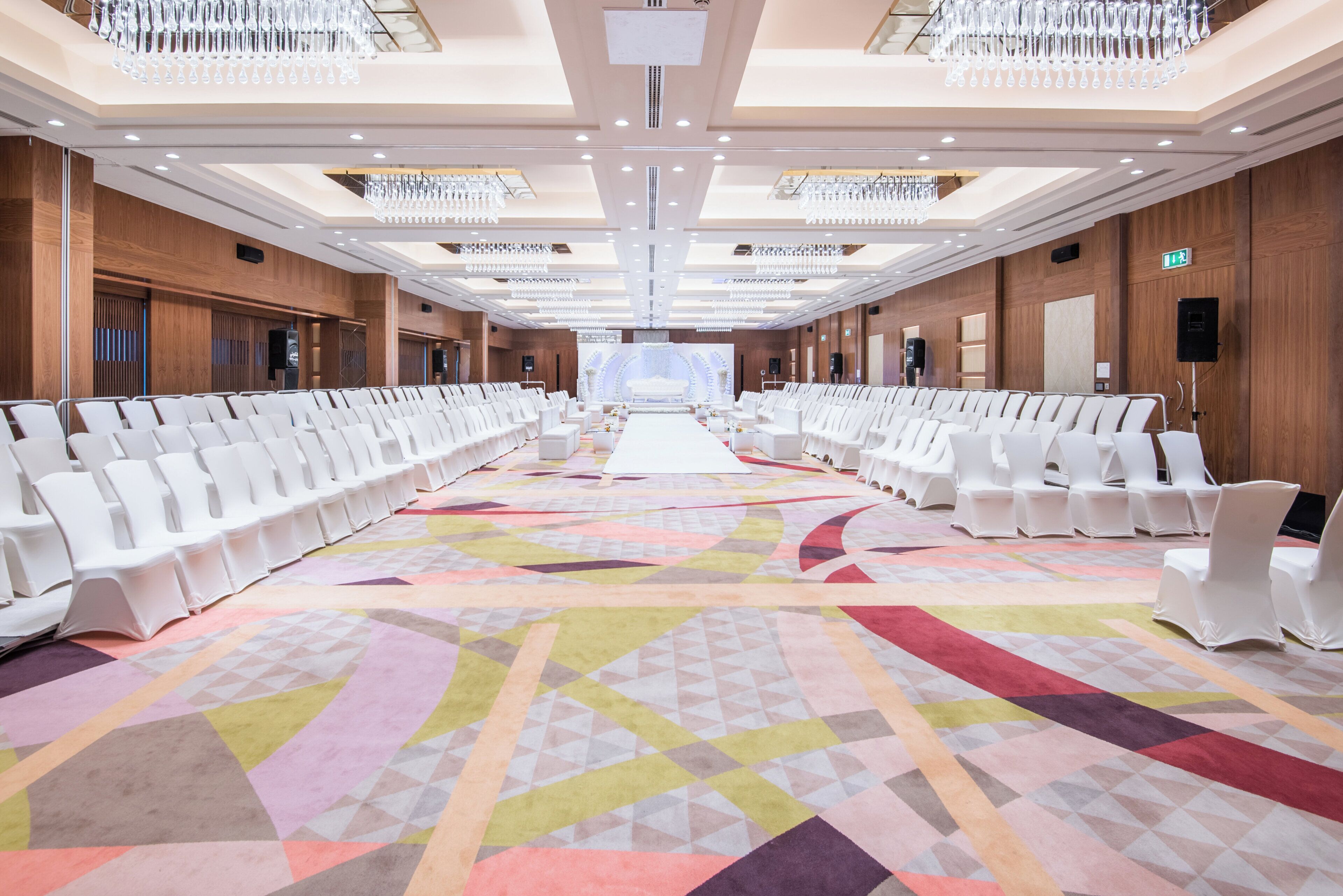A conference room with rows of white chairs, a large screen at the front, and a patterned carpet.
