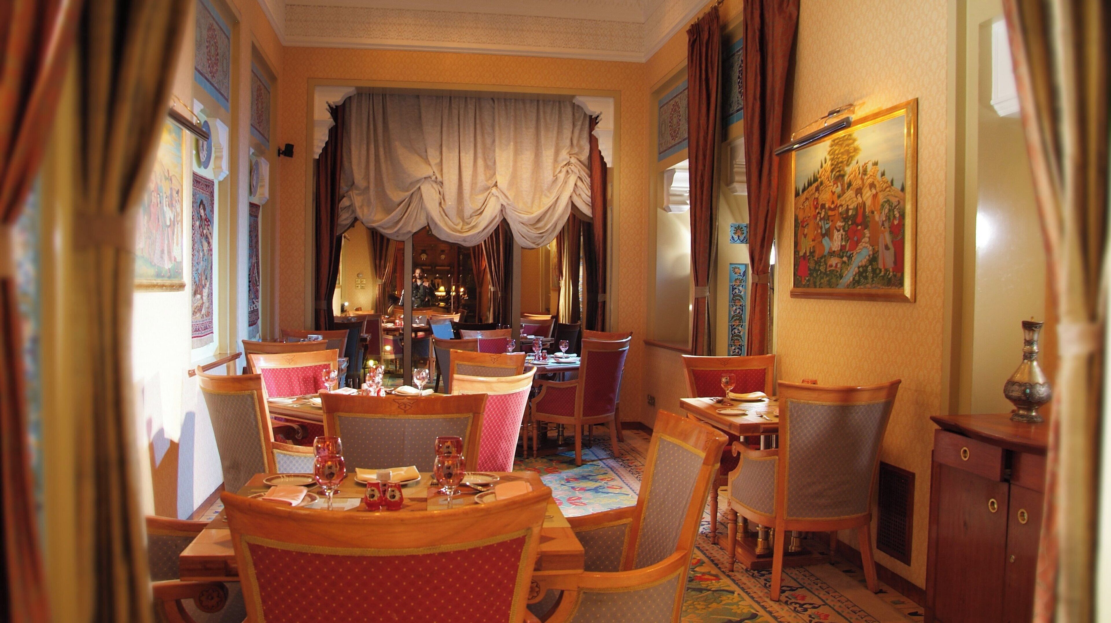 A dining area with multiple tables and chairs, a large painting on the wall, and a patterned carpet.