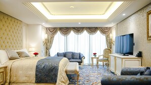 A spacious bedroom with a large bed, a sofa, a television, and a small table. - Crowne Plaza Kuwait Al Thuraya City by IHG (Farwaniya)