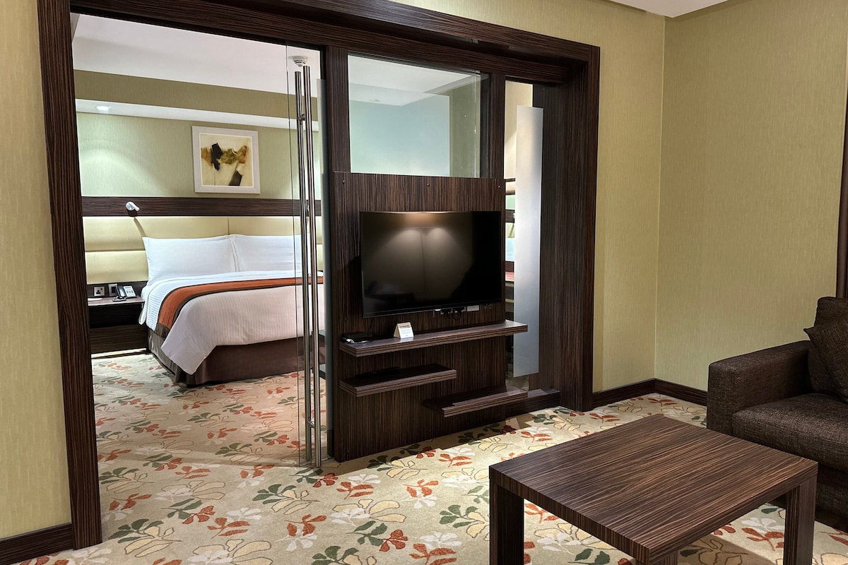 A hotel room with a bed, a television, a sofa, and a floral carpet.