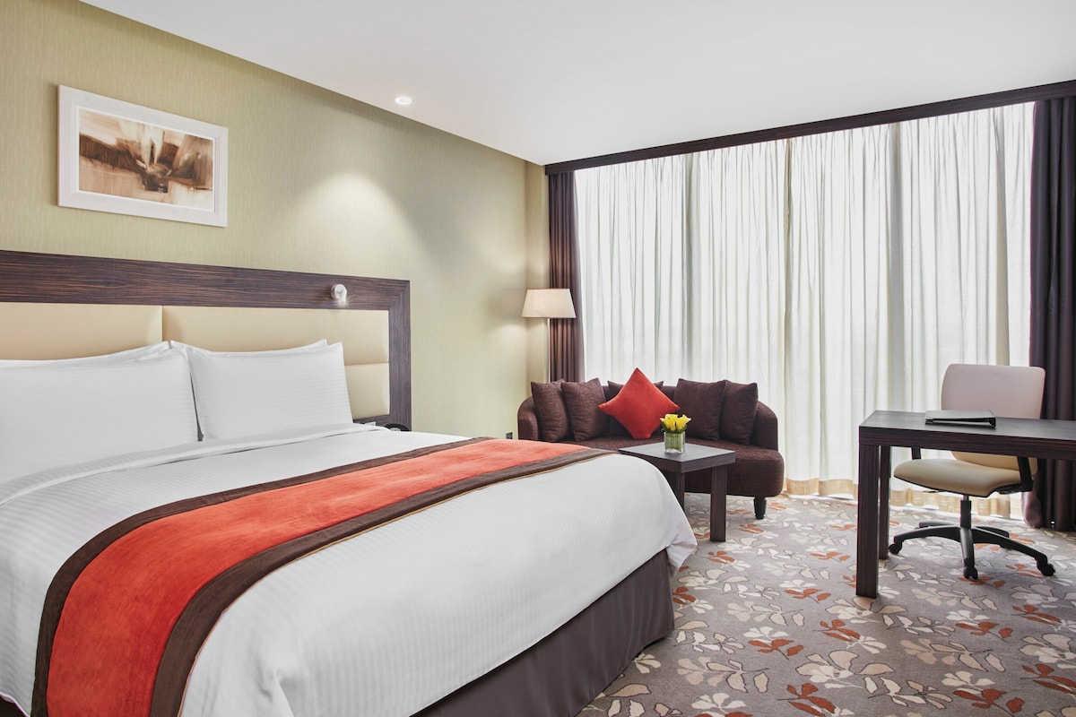 A hotel room with a large bed, a sofa, a desk, and a window with curtains.