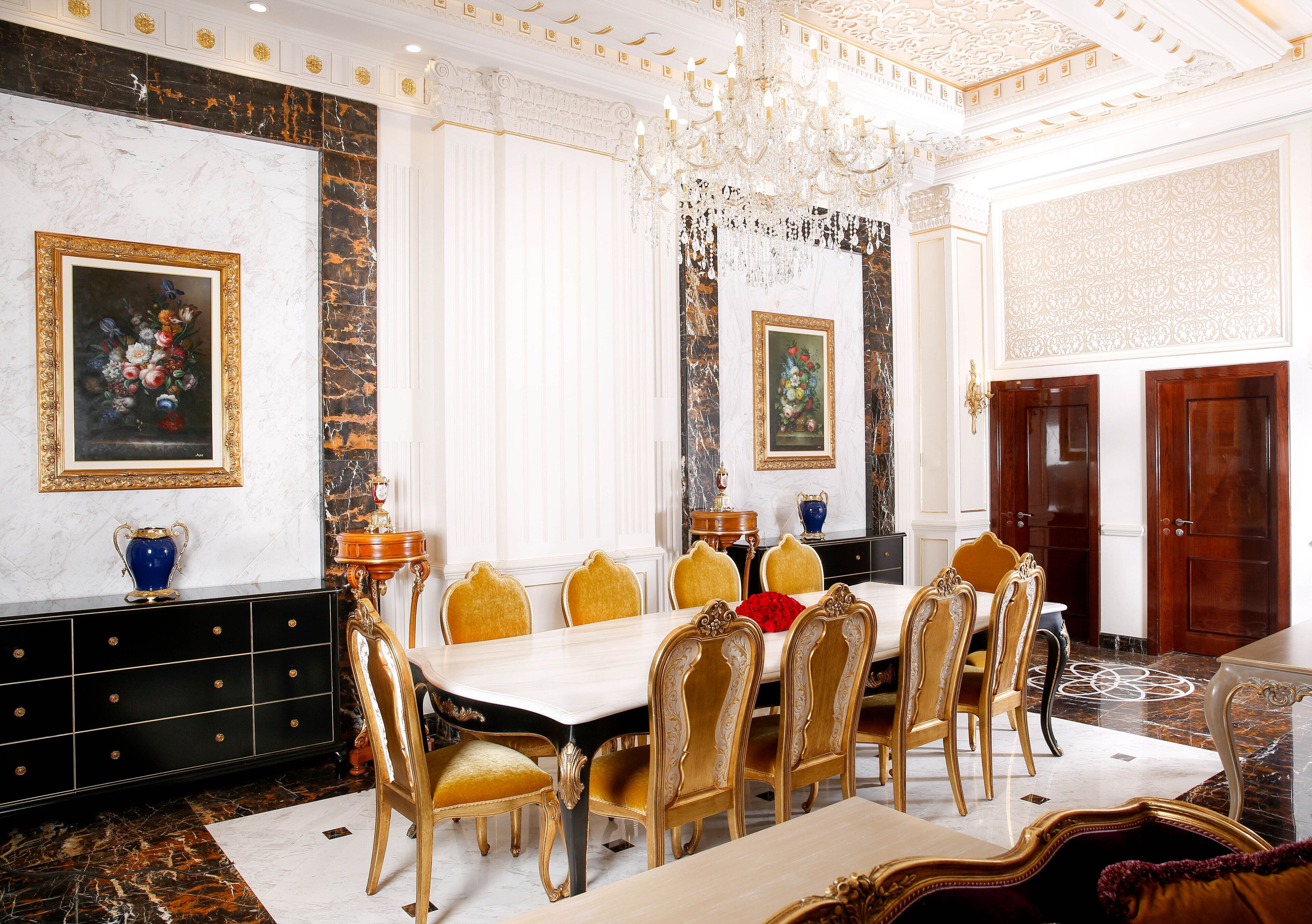 Un comedor elegante con suelo de mármol, sillas doradas, una mesa blanca y decoración elaborada.