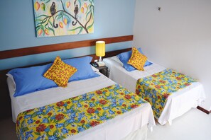 Two single beds with floral bedspreads, a nightstand with a lamp, and a painting on the wall. - Pousada Só Alegria (São Miguel do Gostoso)