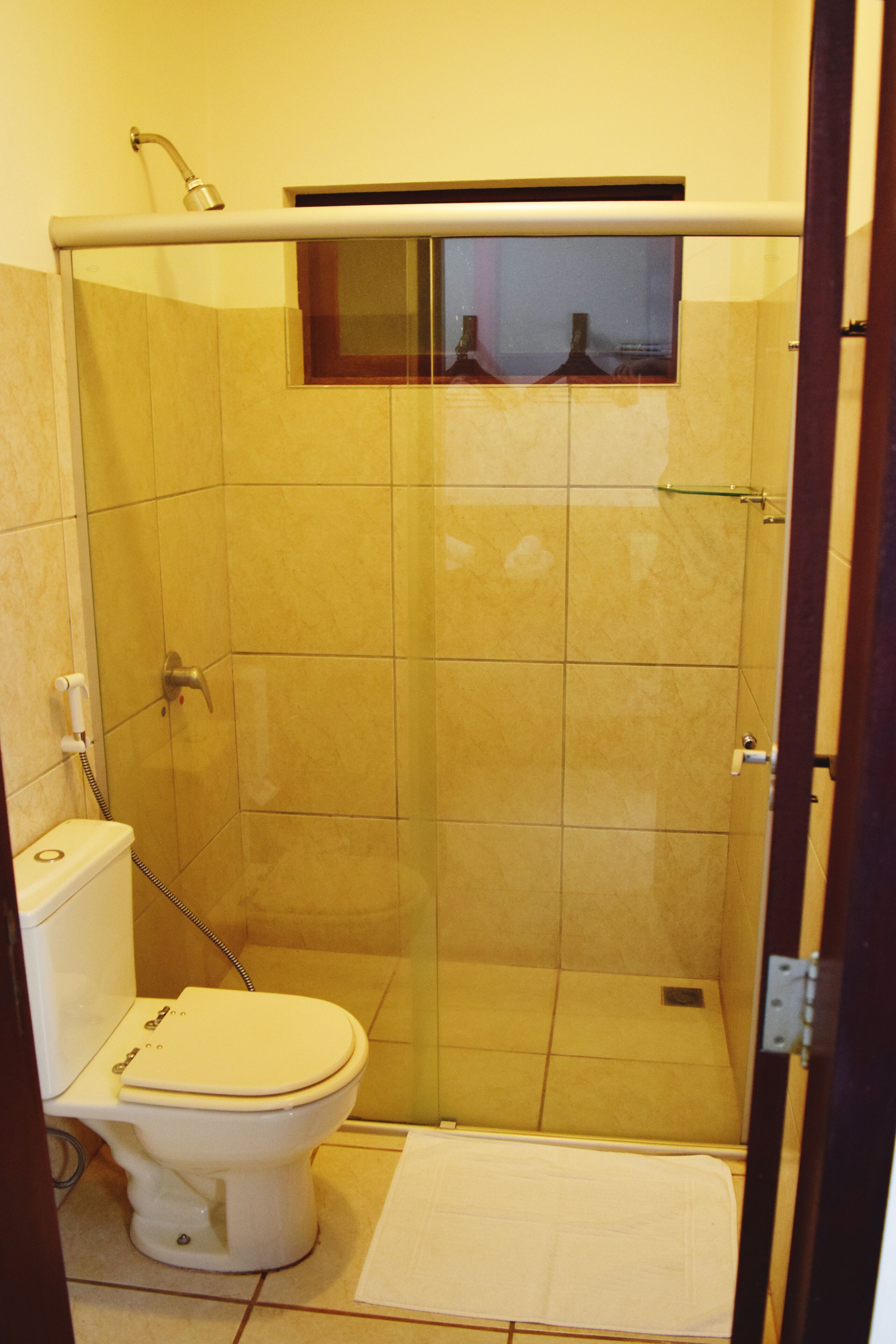 A bathroom with a shower, toilet, and a small window.