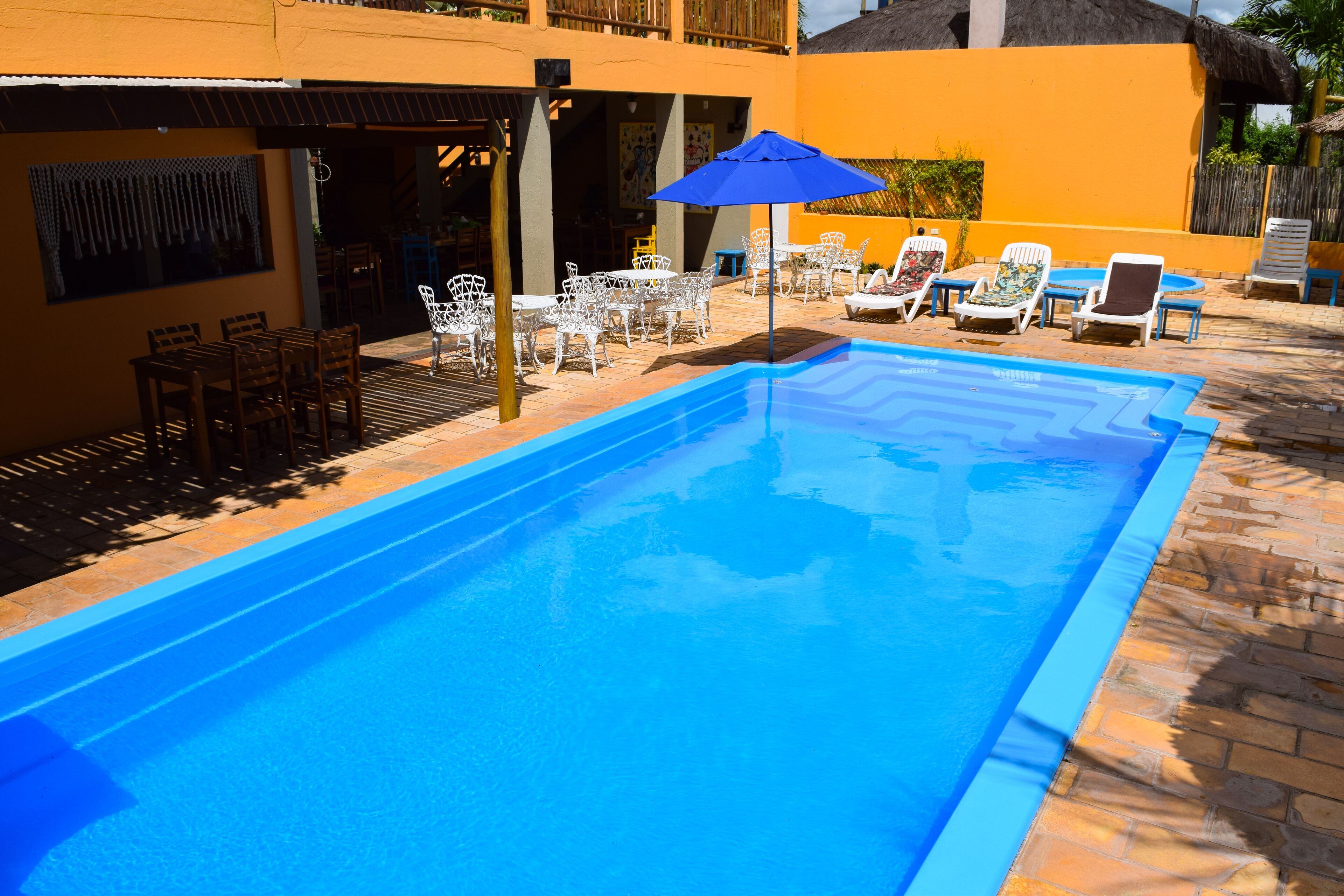 A swimming pool with lounge chairs and umbrellas, surrounded by a patio area with tables and chairs.