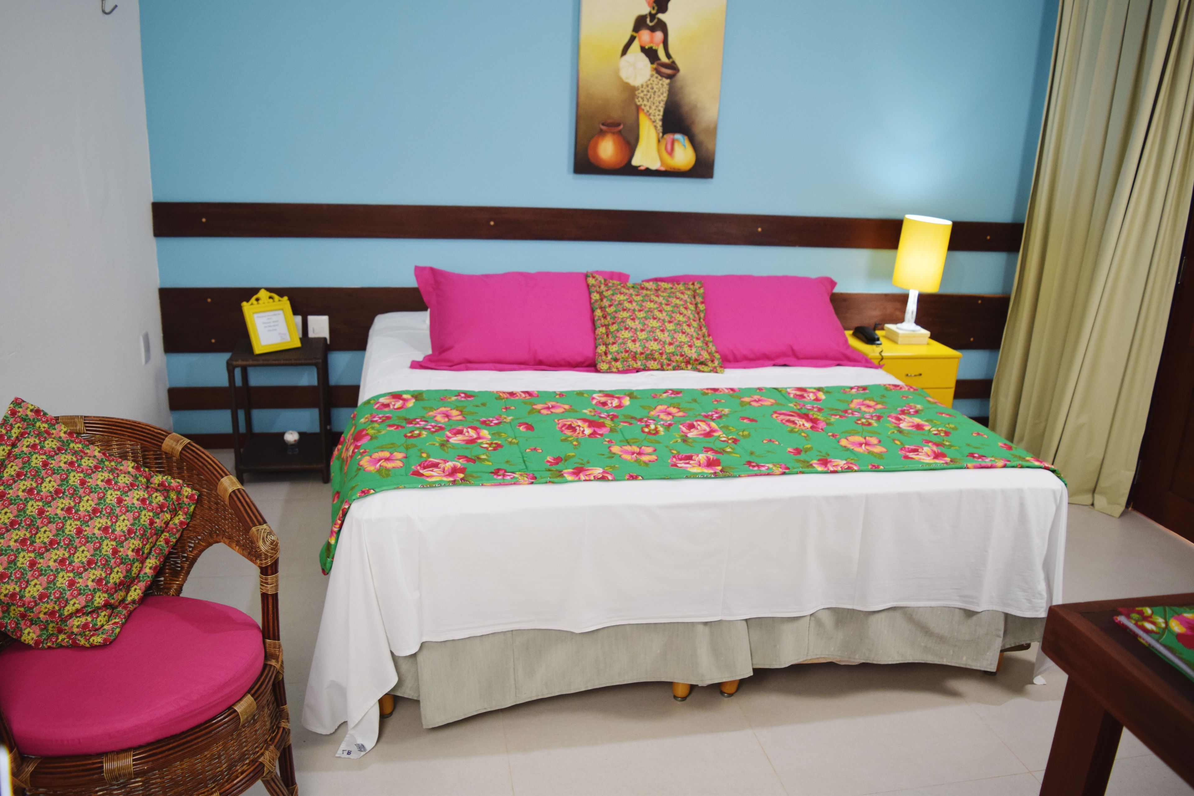 A hotel room with a bed, a chair, a nightstand, and a painting on the wall.