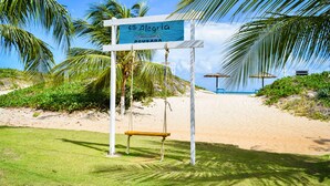 A beach entrance sign with a swing, palm trees, and a sandy beach. - Pousada Só Alegria (São Miguel do Gostoso)